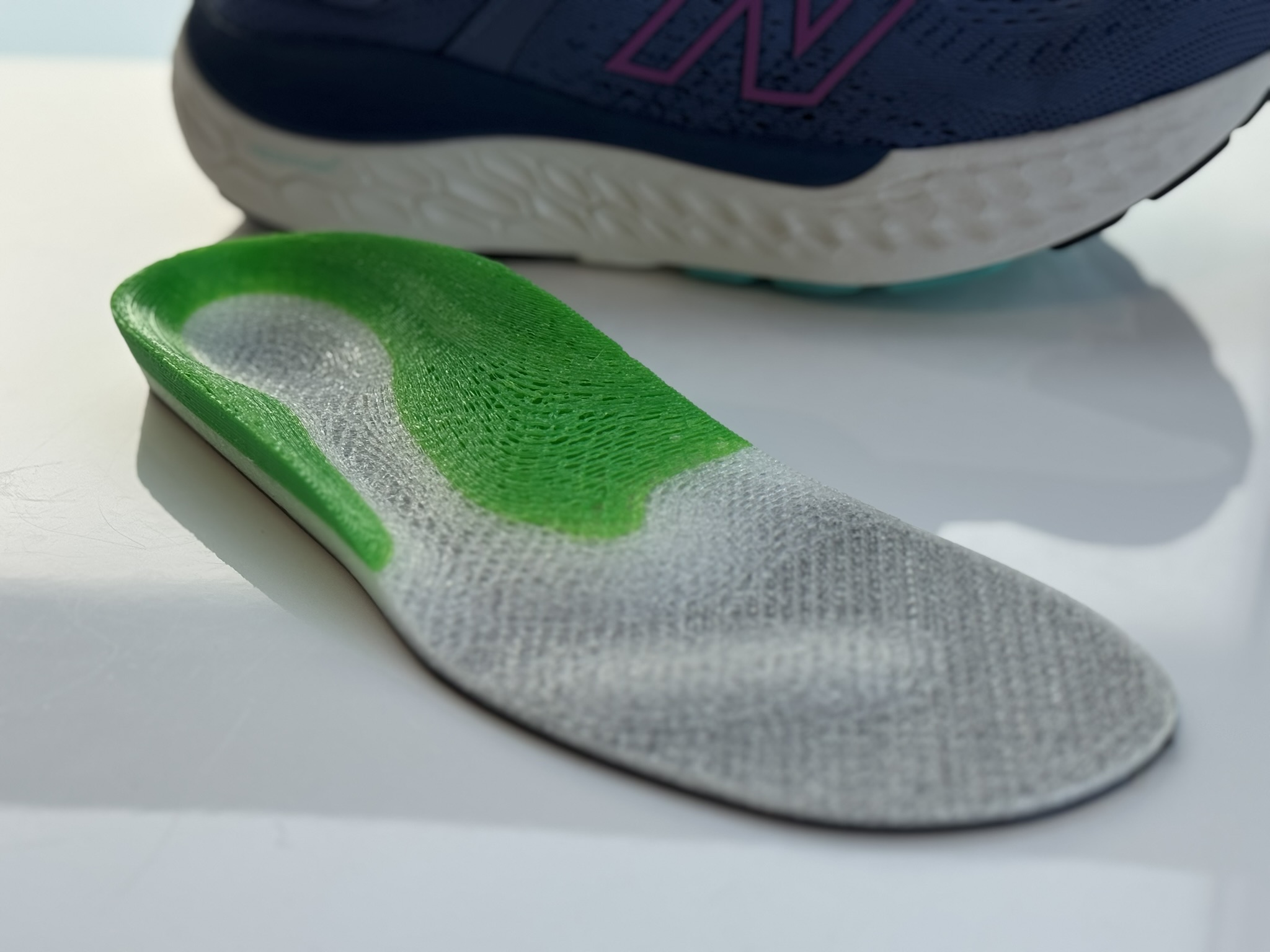 Multi-density 3D printed orthotic insole beside New Balance runner